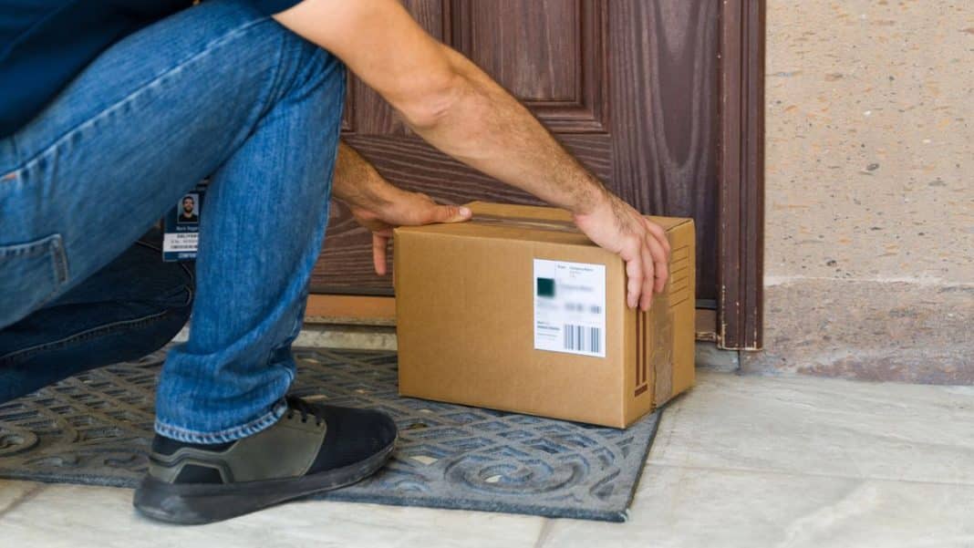 Mężczyzna sięga po paczkę pozostawioną pod drzwiami mieszkania.
