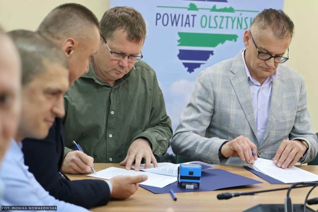 Podpisanie um&oacute;w na modernizację dr&oacute;g w gminach pod Olsztynem, na zdjęciu urzędnicy przy stole.