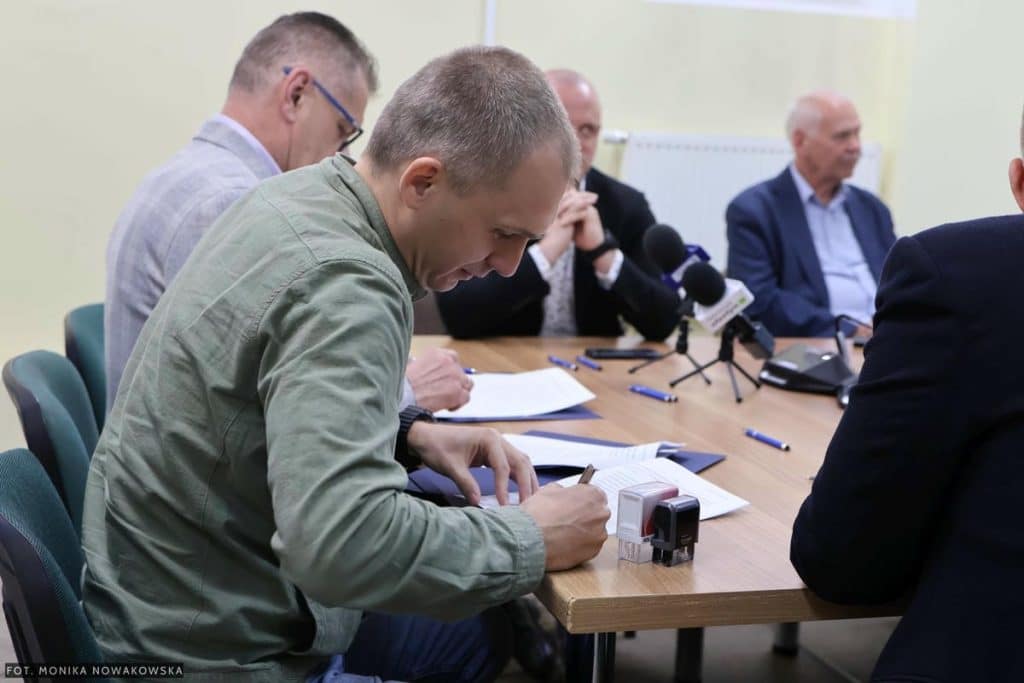 Mężczyzna podpisuje dokumenty podczas spotkania z innymi osobami przy stole.
