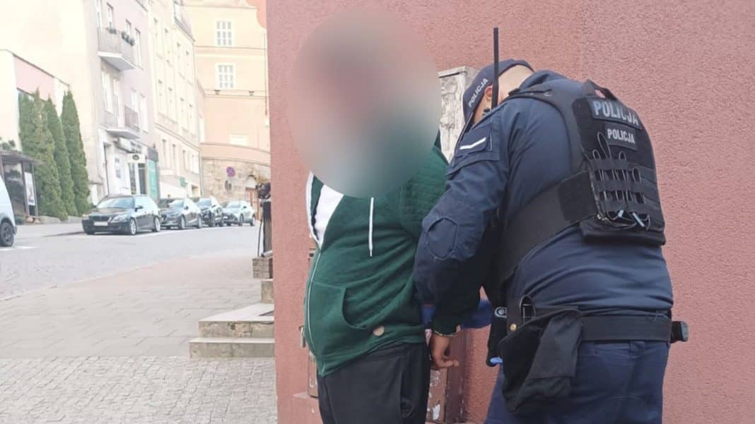 Policjant zatrzymuje mężczyznę na ulicy, na tle budynków i samochodów.