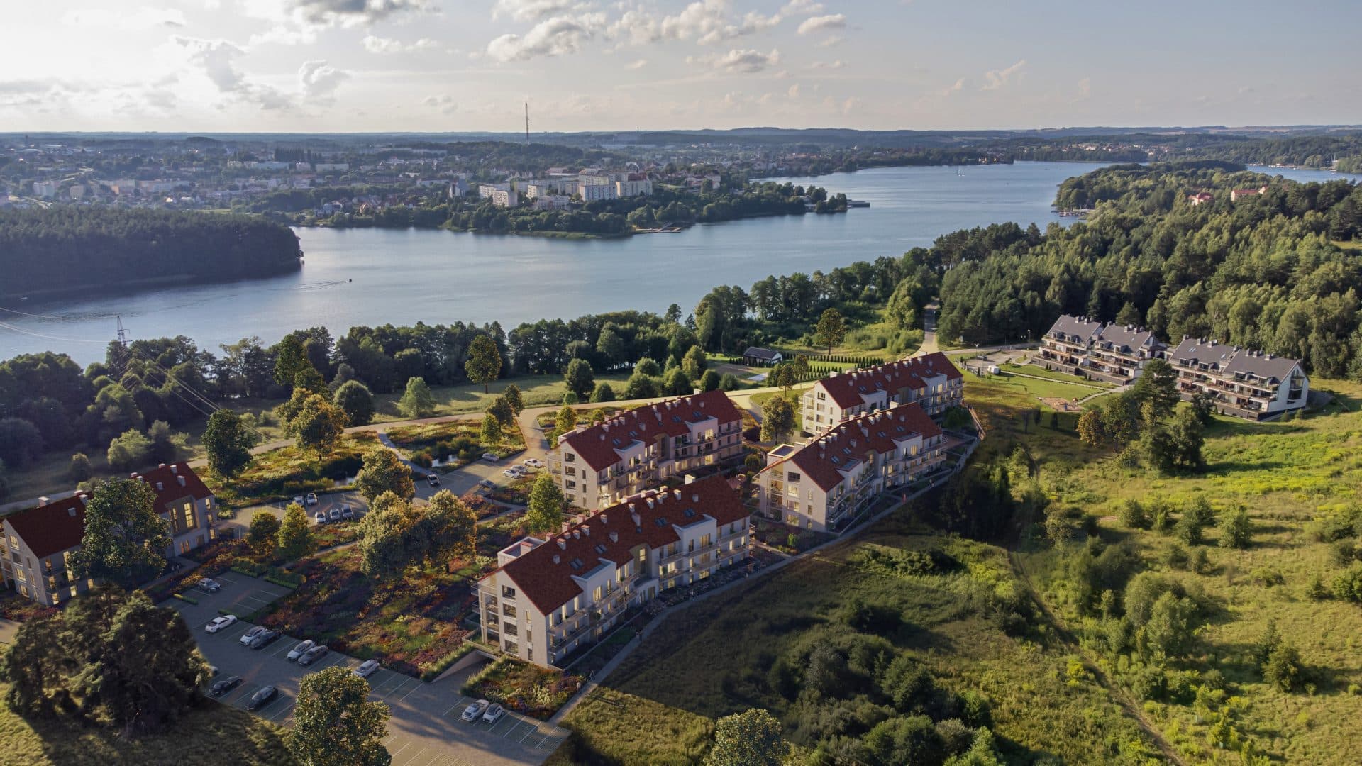 Widok na nowoczesne apartamenty nad jeziorem Czos w Mrągowie, otoczone zielenią i lasem.