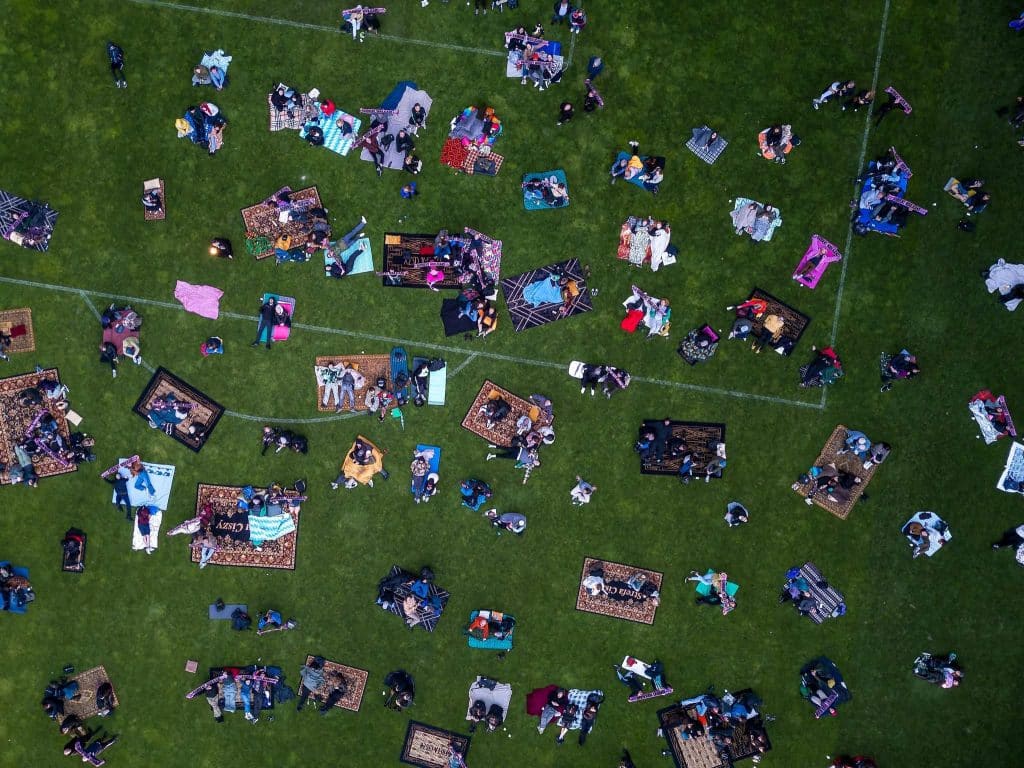 Zdjęcie z lotu ptaka przedstawia grupę ludzi na trawie, siedzących na dywanach i kocach podczas festiwalu.