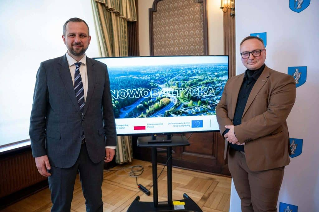 Dw&oacute;ch mężczyzn w garniturach i marynarkach stoją obok ekranu z mapą Olsztyna i napisem Nowobałtycka.