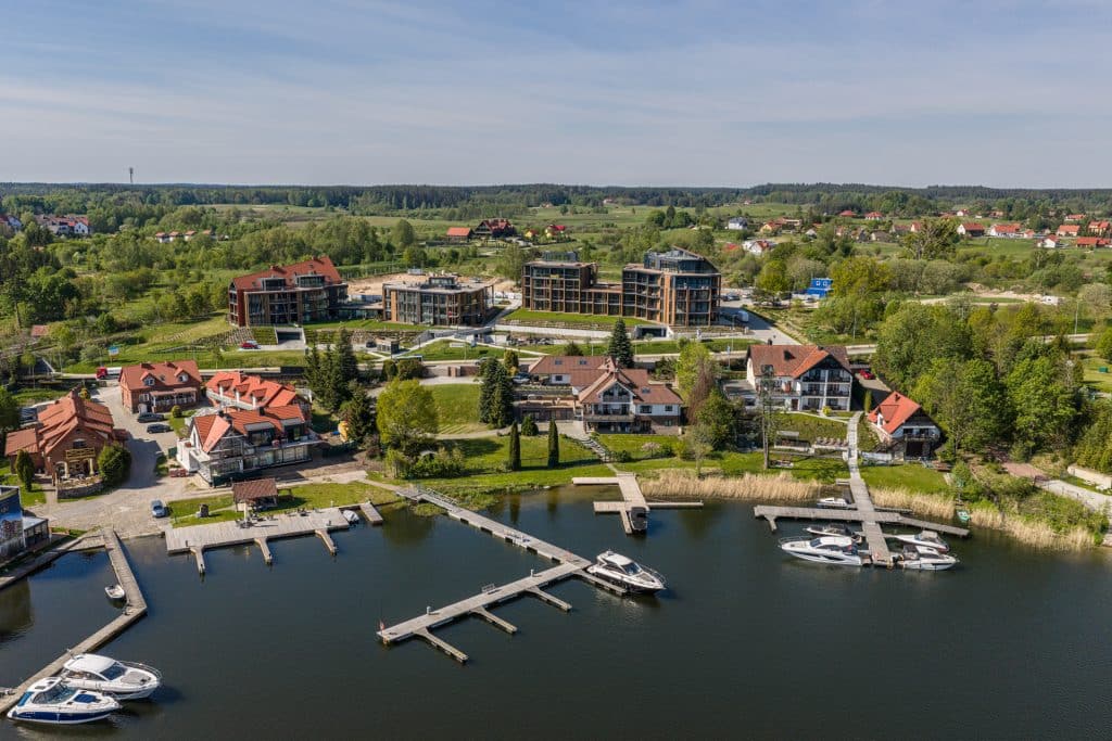Widok na luksusowe apartamenty nad jeziorem na Mazurach, z mariną i zielonym otoczeniem.