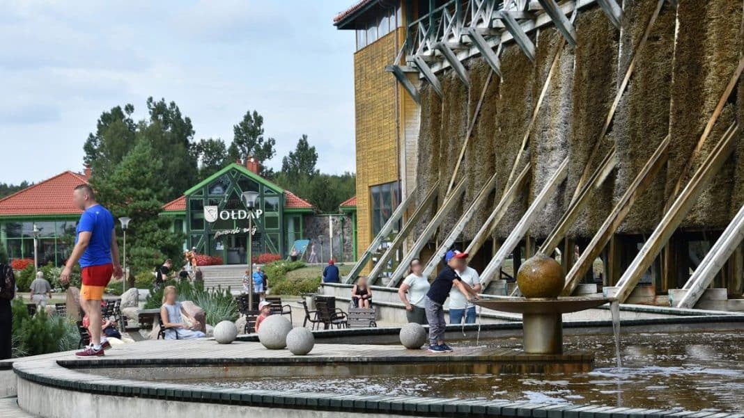 Tężnie solankowe w Gołdapi z odwiedzającymi na zewnątrz, w tle budynek uzdrowiska i zielone drzewa.