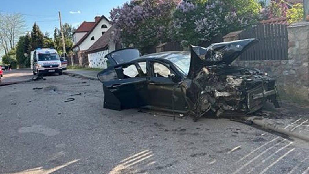 Rozbity samochód BMW o ogrodzenie, na miejscu policja i służby ratunkowe.