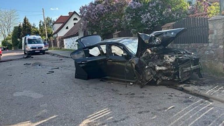 Rozbity samochód BMW o ogrodzenie, na miejscu policja i służby ratunkowe.