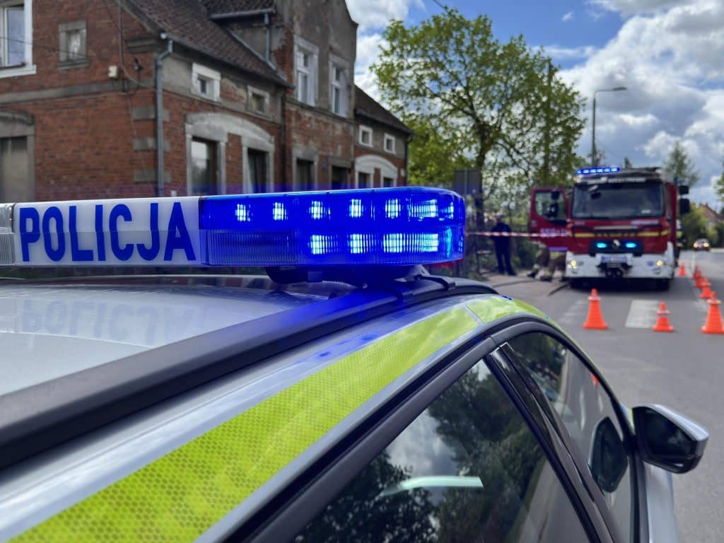 Policja i straż pożarna na miejscu pożaru w mieście, widok na niebieskie światła na radiowozie.