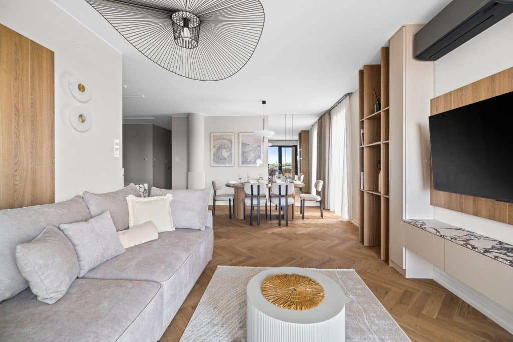 Wnętrze nowoczesnego apartamentu z dużym salonem, drewnianymi elementami i dużymi oknami z zasłonami.