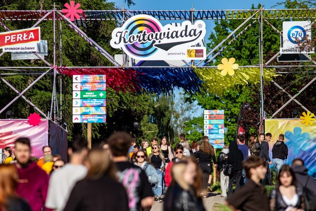 Tłum ludzi na terenie festiwalu Kortowiada, widoczny wejście z dużym logo i kolorowe dekoracje.