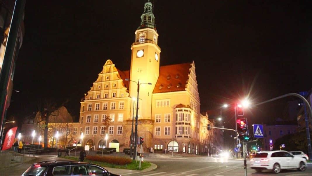 Wieża ratusza oświetlona nocą, w tle ciemne niebo i ruchliwe ulice.
