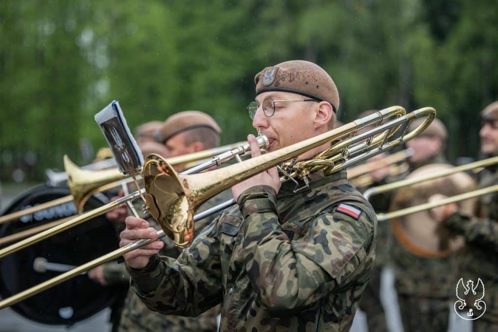 Żołnierz w mundurze grający na trąbce podczas uroczystości wojskowej na zewnątrz.