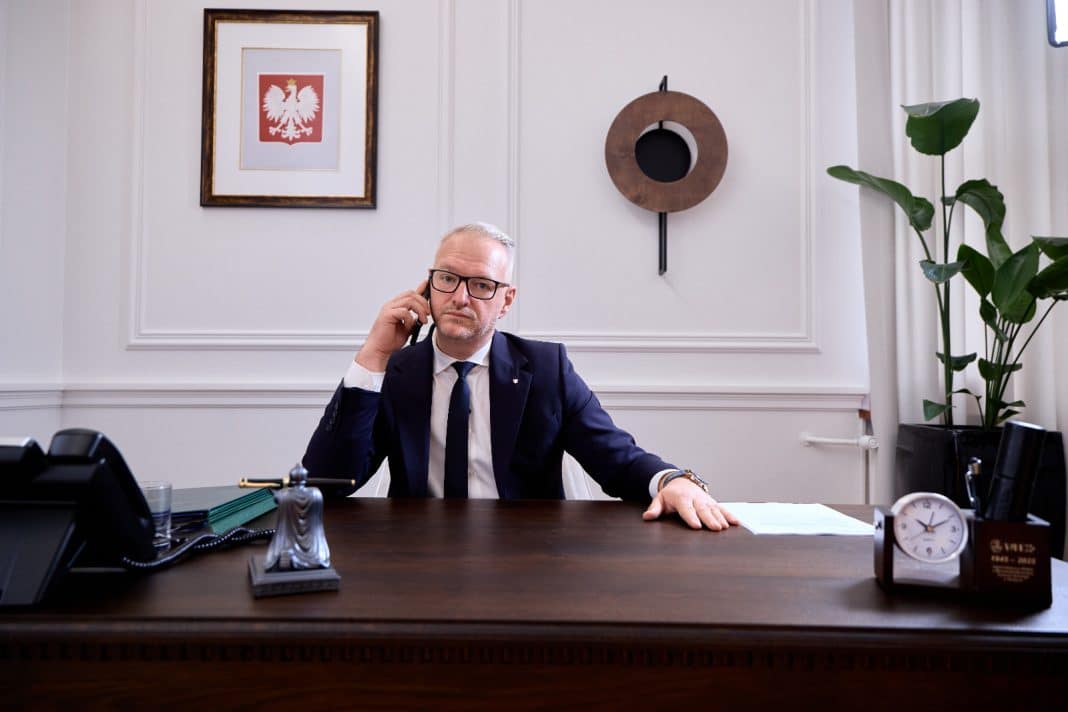 Mężczyzna w biurze rozmawia przez telefon, za nim obraz orła na ścianie.