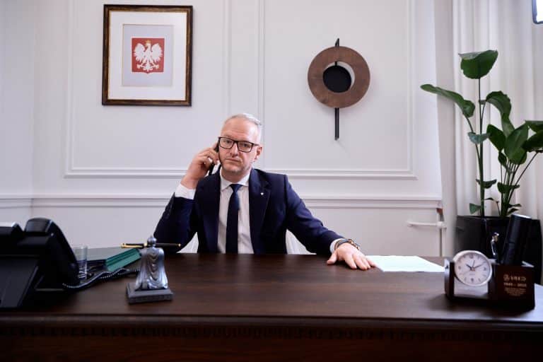 Mężczyzna w biurze rozmawia przez telefon, za nim obraz orła na ścianie.