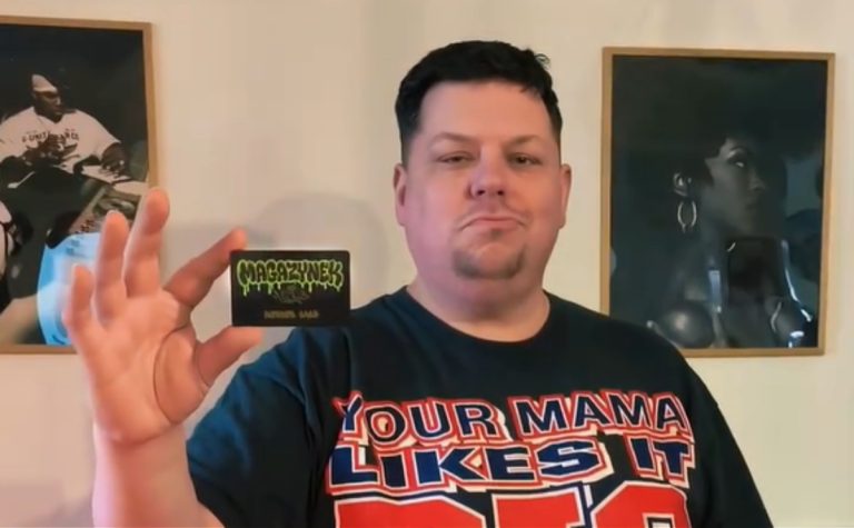 Mężczyzna trzyma wizytówkę Magazynku Vintage, w tle zdjęcia na ścianie.