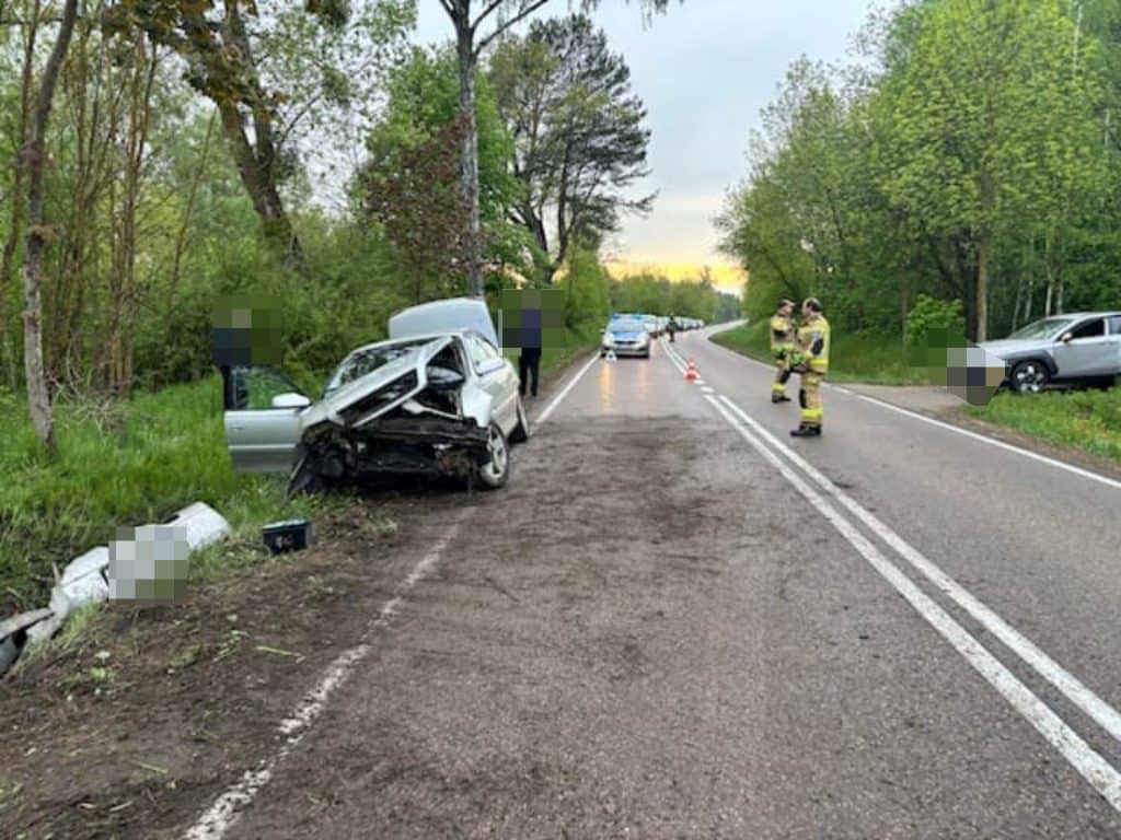 Rozbity samoch&oacute;d na poboczu drogi krajowej, policjanci i strażacy na miejscu wypadku.