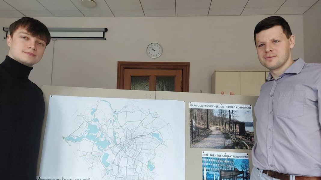 Dw&oacute;ch mężczyzn prezentuje plakat z mapą i koncepcjami rozwoju infrastruktury rowerowej w Olsztynie.