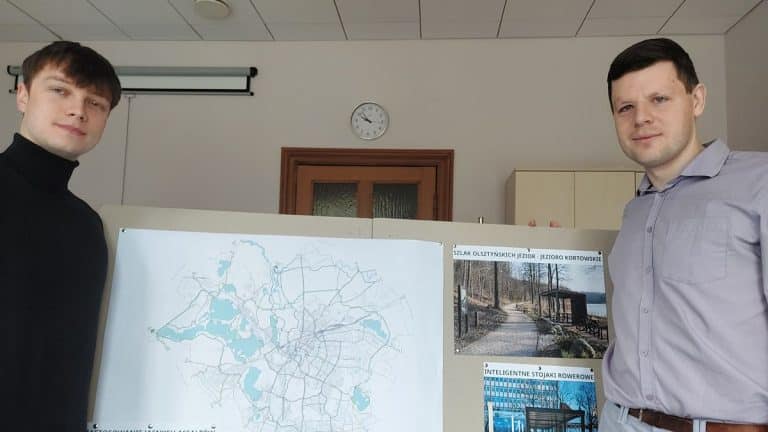 Dw&oacute;ch mężczyzn prezentuje plakat z mapą i koncepcjami rozwoju infrastruktury rowerowej w Olsztynie.