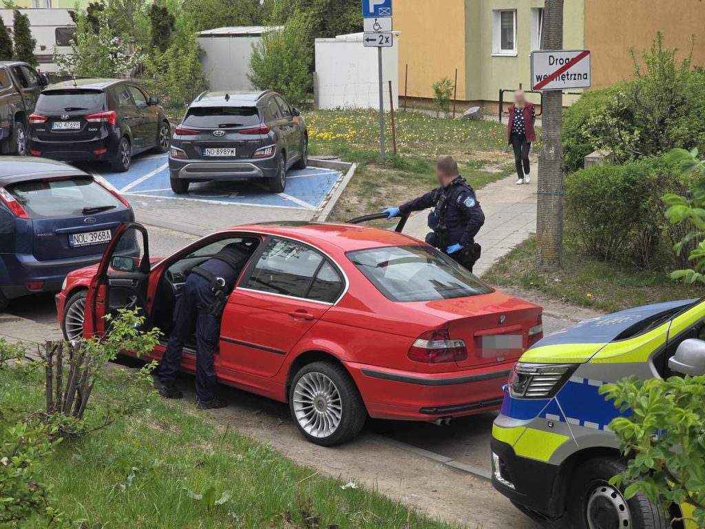 Policjant otwiera drzwi czerwonego BMW podczas akcji w centrum Olsztyna.