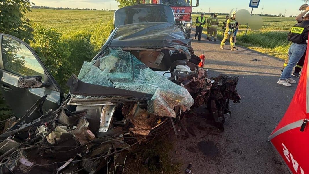 Rozbity samochód BMW po wypadku na drodze, w tle służby ratunkowe i straż pożarna.