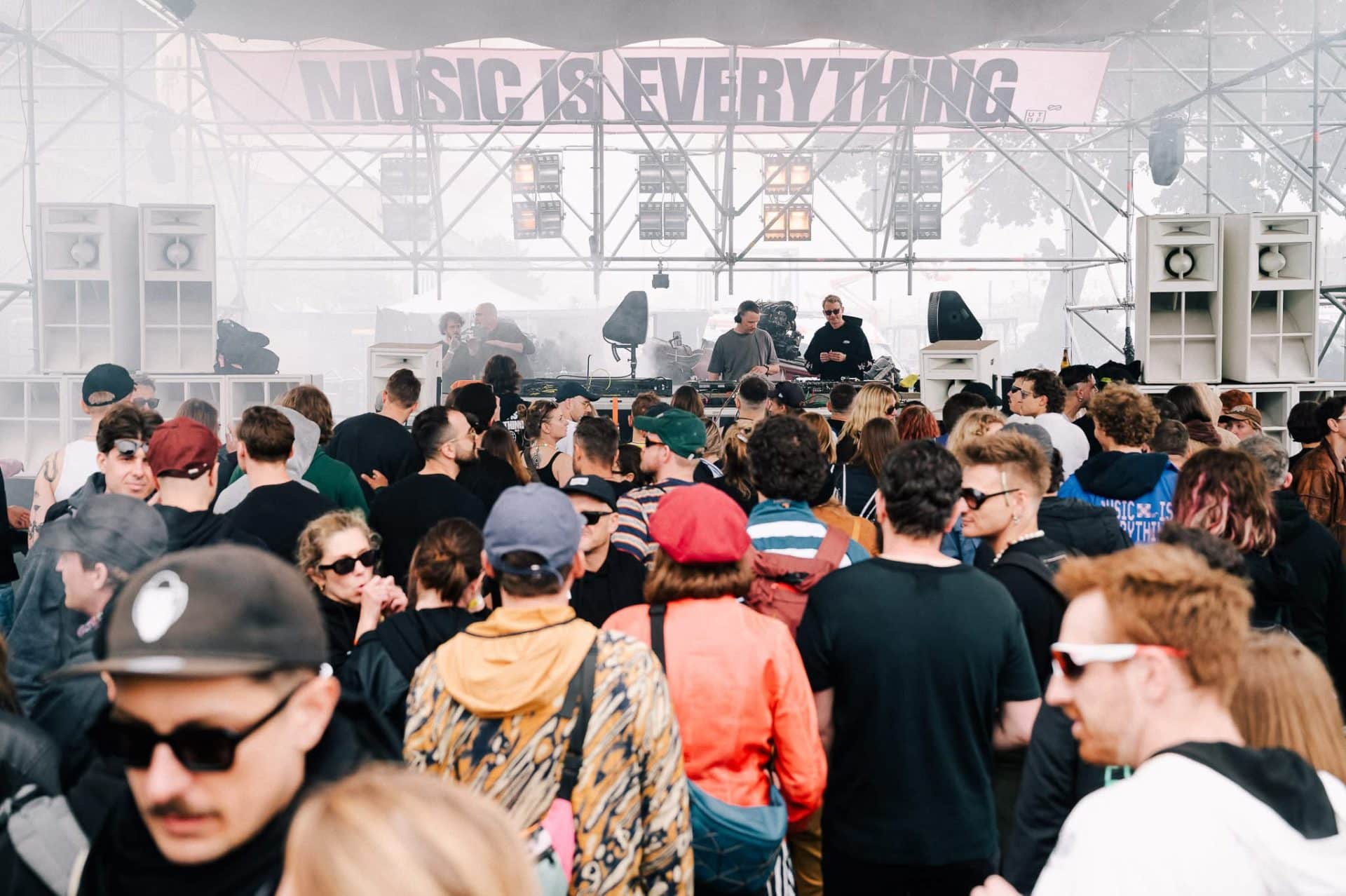 Tłum ludzi na festiwalu muzyki elektronicznej, scena z DJ-ami i napis 'Music is Everything' w tle.