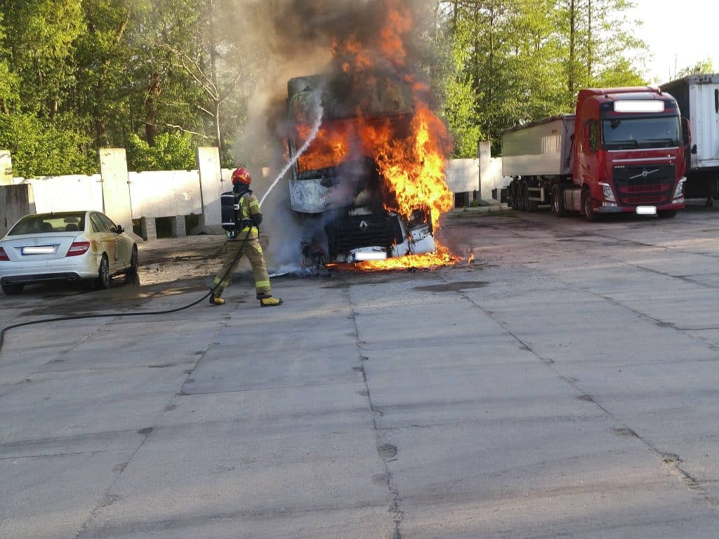Strażak gasi pożar ciężar&oacute;wki na parkingu, z kabiny unosi się dym i płomienie.