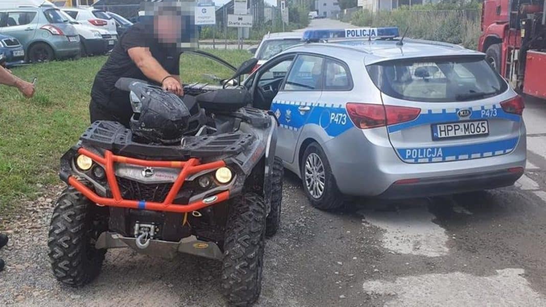 Starszy mężczyzna zatrzymany przez policję przy quadzie, obok radiow&oacute;z, w tle inne pojazdy na parkingu.