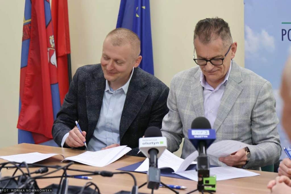 Dwa mężczyźni podpisują umowy na inwestycje drogowe podczas konferencji prasowej.