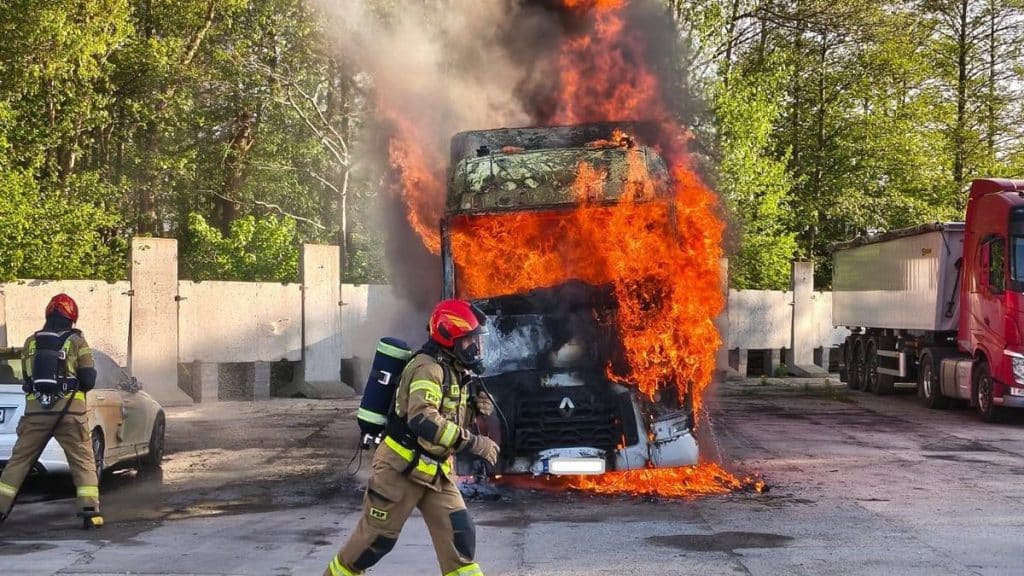 Pożar ciężar&oacute;wki na parkingu w Braniewie, płomienie i dym unoszące się nad pojazdem.