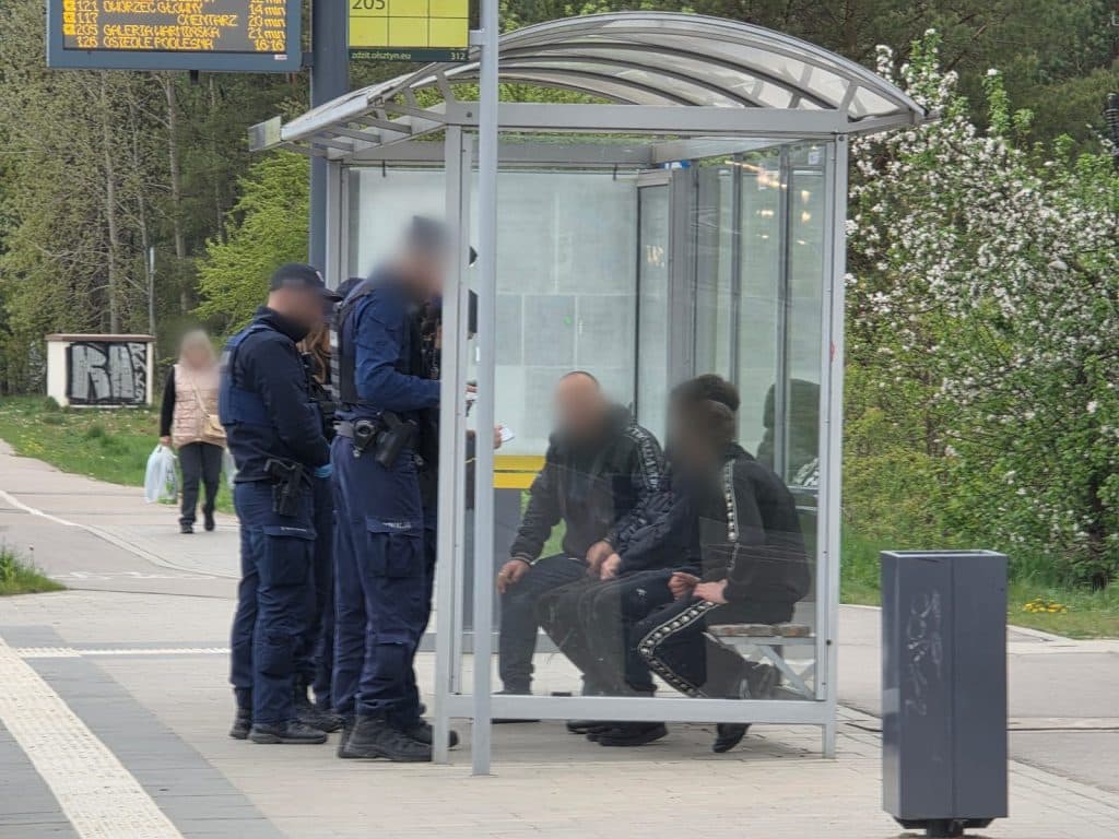 Grupa policjant&oacute;w rozmawia z dwoma osobami w przystanku autobusowym na osiedlu Pieczewo.