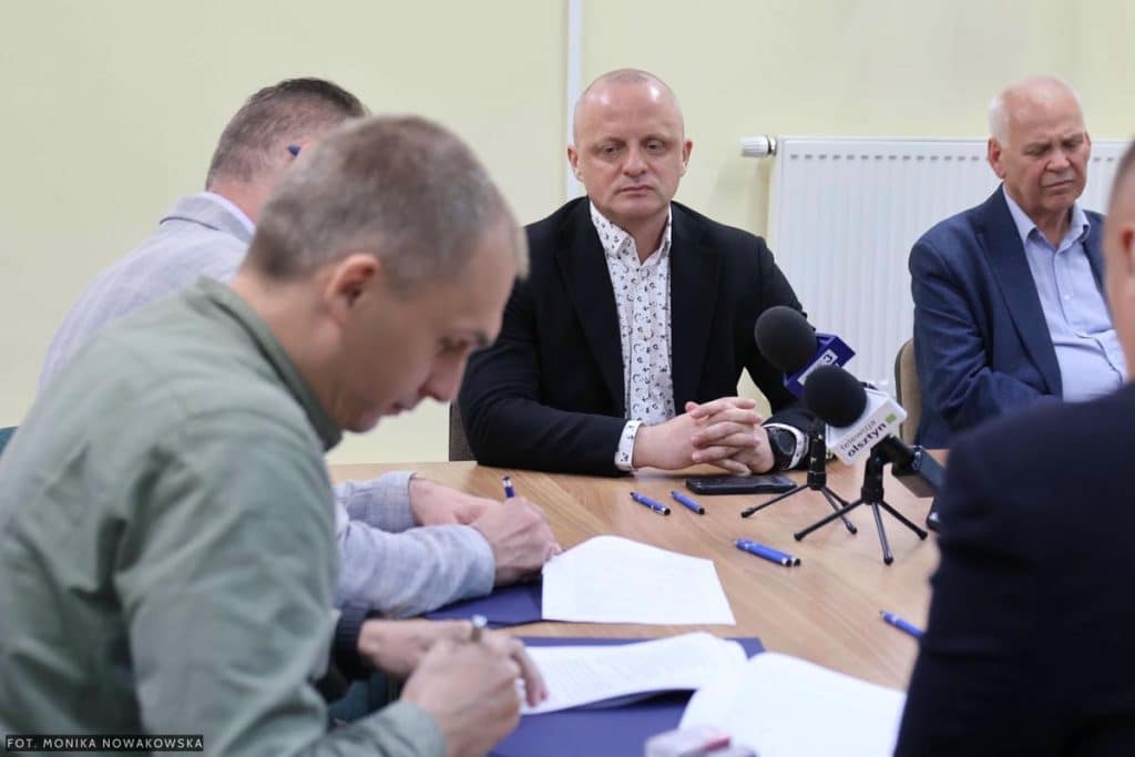 Zdjęcie przedstawia grupę os&oacute;b podczas podpisywania um&oacute;w na inwestycje drogowe w powiecie olsztyńskim.
