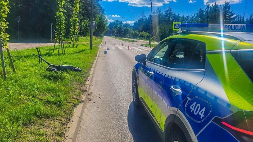 Rozbity rower na poboczu i radiowóz policji na drodze podczas akcji ratunkowej.