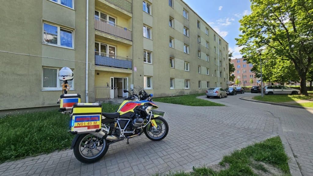Na zdjęciu budynek mieszkalny z parkingiem i motocyklami ratunkowymi przed wejściem.