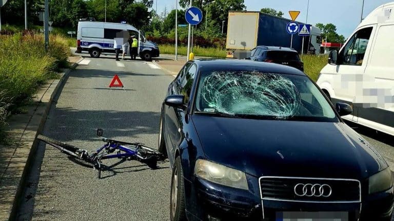 Wypadek na rondzie w Ełku, uszkodzony rower i rozbity samochód Audi, policja na miejscu.