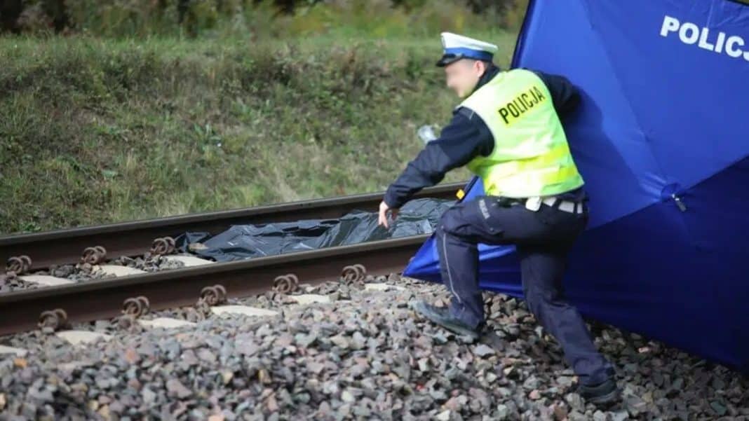 Policjant na miejscu wypadku na torach, obok leży ciało przykryte czarną folią.