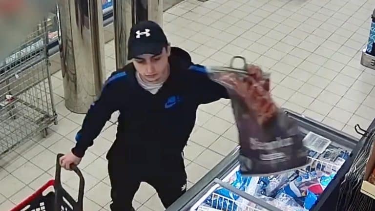 Mężczyzna w czapce i czarnej kurtce z niebieskimi elementami, trzymający torbę, robi zakupy w sklepie.