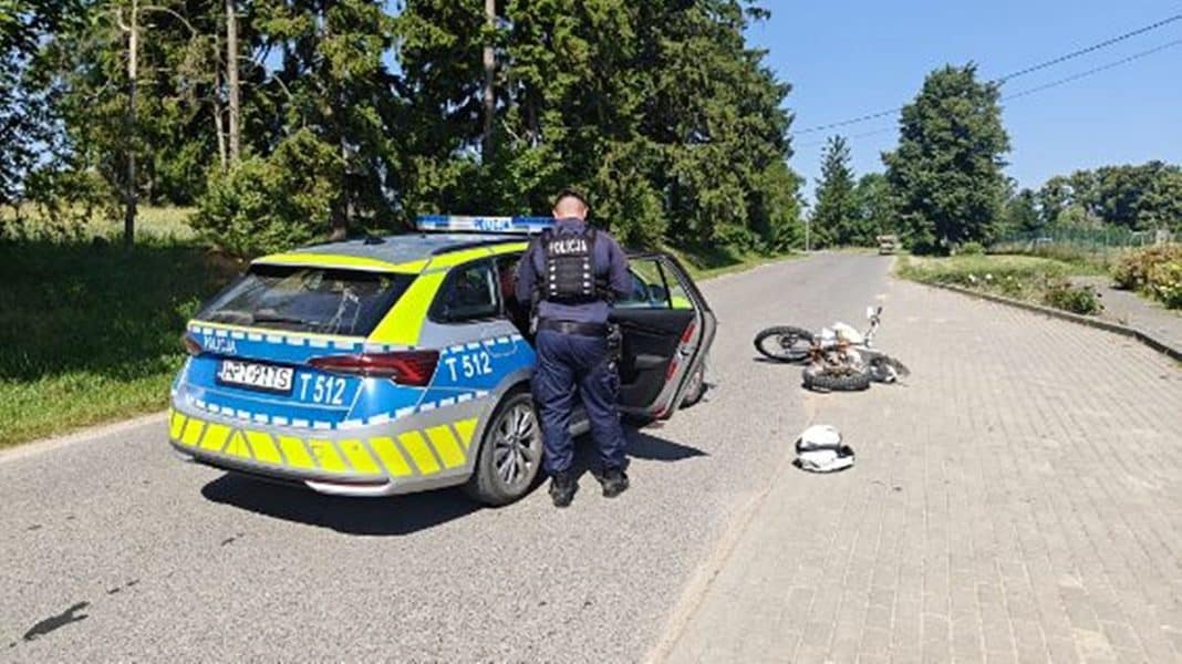 Policjant przy radiowozie na ulicy, obok rozbity motocykl i kask.