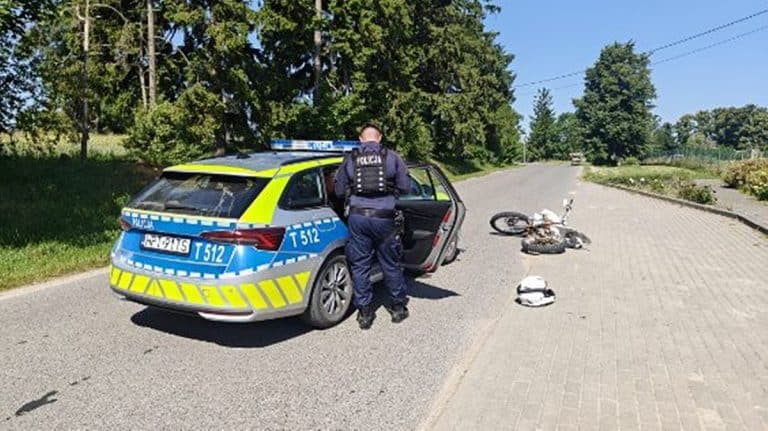 Policjant przy radiowozie na ulicy, obok rozbity motocykl i kask.