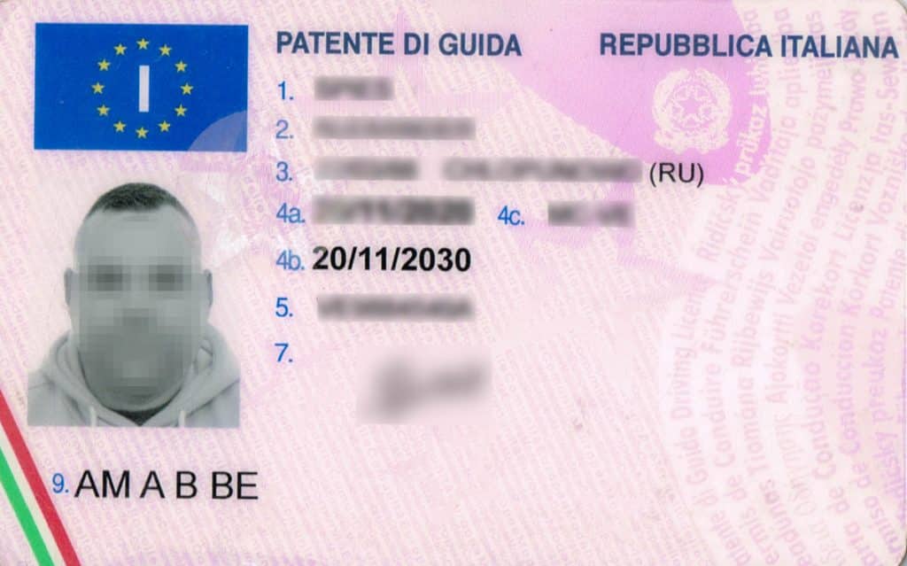 Zdjęcie włoskiego prawa jazdy z widocznym zdjęciem i danymi osobowymi, na tle tekstu.