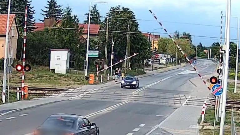 Kobieta wjechała na przejazd kolejowy, gdy zamykały się rogatki, w tle samochody i przejazd kolejowy.