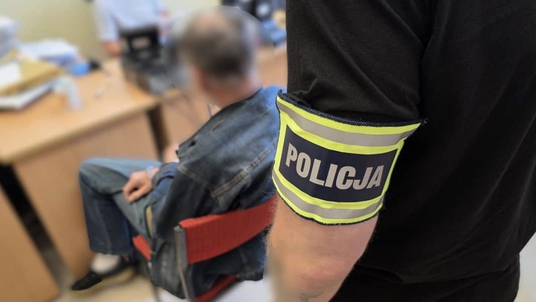 Mężczyzna w policyjnym opasce trzyma chłopca na rękach, w tle biurko i dokumenty.
