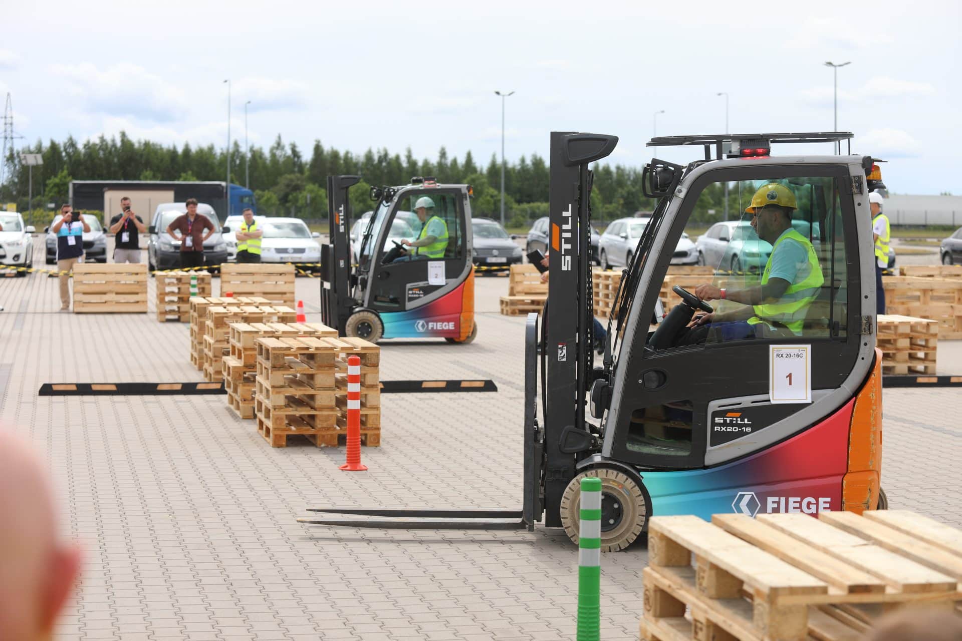 Operatorzy wózków widłowych rywalizują podczas zawodów w Ameryce koło Olsztynka, na tle ustawionych palet i słupków.