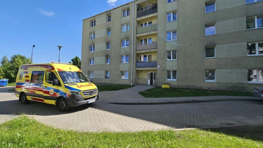 Ambulans zaparkowany przed blokiem mieszkalnym w Olsztynie, w tle budynek wielorodzinny.