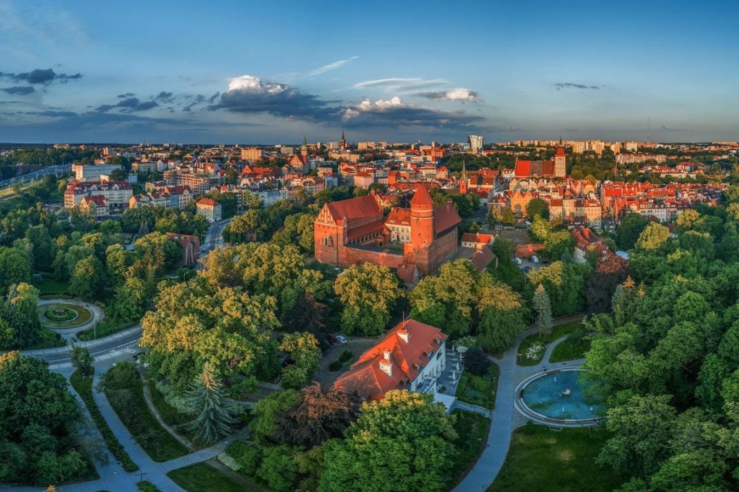 Widok na starówkę i zamek w malowniczym mieście otoczonym zielenią, podczas zachodu słońca.