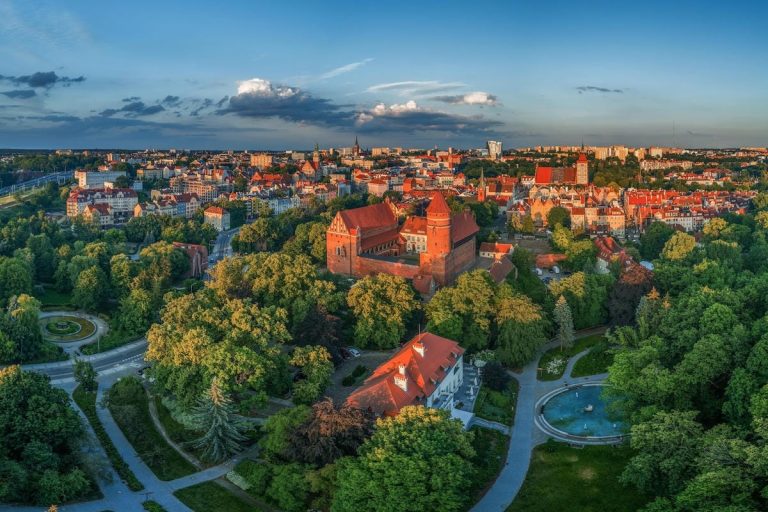 Widok na starówkę i zamek w malowniczym mieście otoczonym zielenią, podczas zachodu słońca.