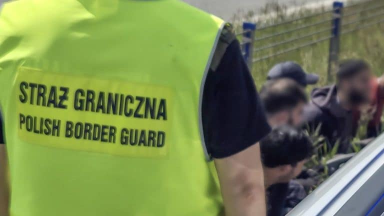Funkcjonariusze Straży Granicznej zatrzymują pasażerów w samochodzie na drodze, w tle widoczny bagażnik.