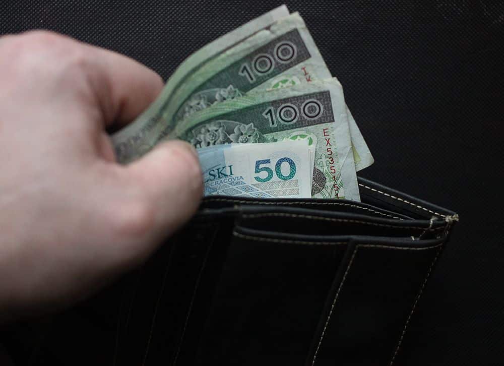 Portfel z banknotami 50 i 100 zł, trzymany nad czarnym tłem.