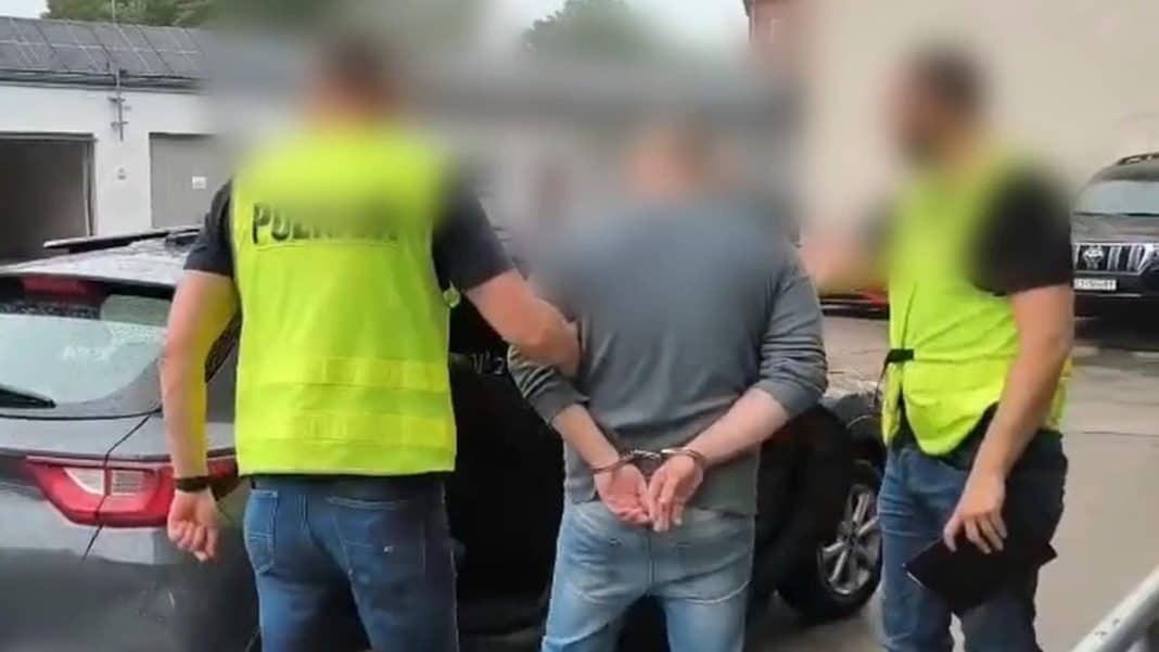 Policjanci zatrzymują podejrzanego mężczyznę na ulicy, wokół radiowóz i dwie osoby w odblaskowych kamizelkach.