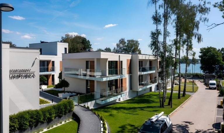 Nowoczesny kompleks apartamentów nad jeziorem z zielonymi terenami i ścieżkami spacerowymi.