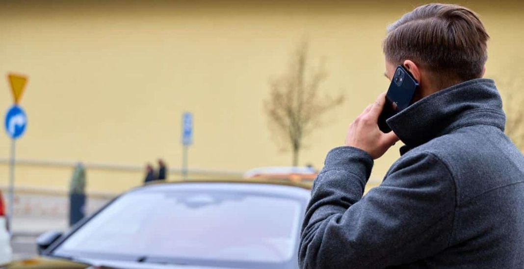 Mężczyzna rozmawia przez telefon na ulicy, w tle samochody i budynek.